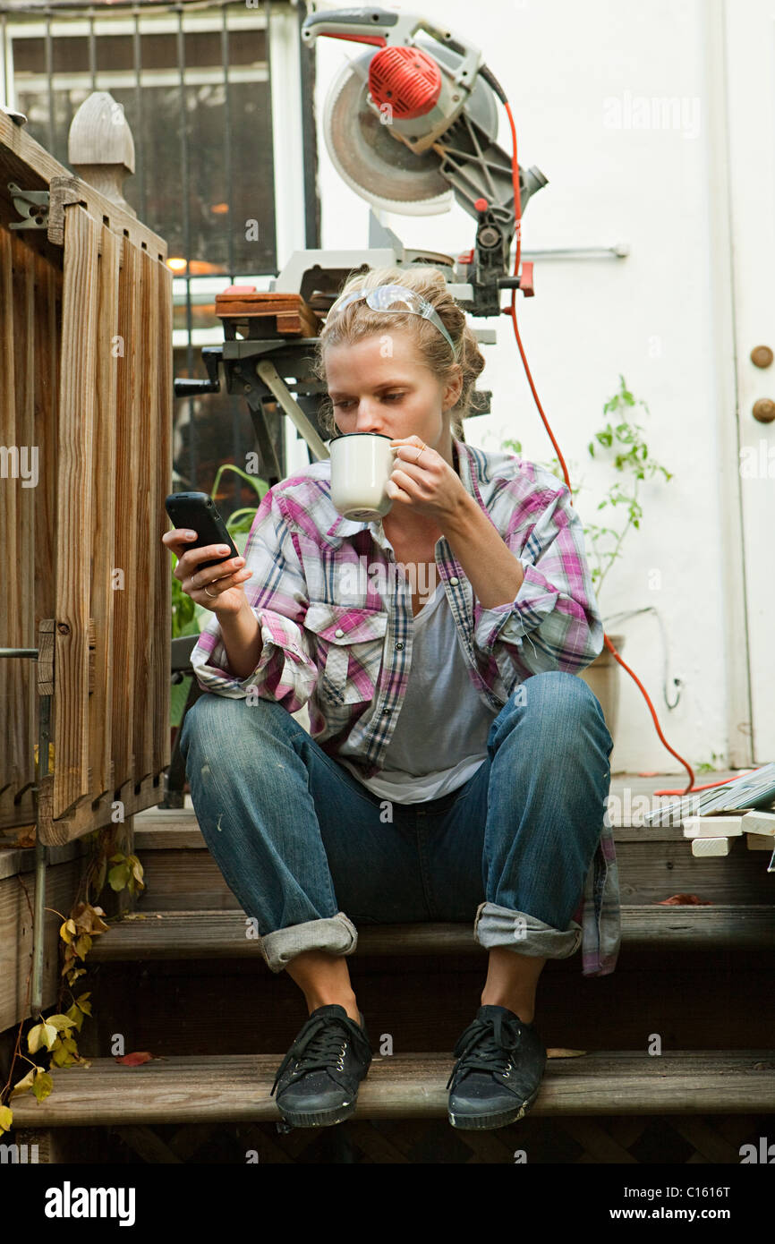 Femme assise sur les marches avec le smartphone de boire une boisson chaude Banque D'Images