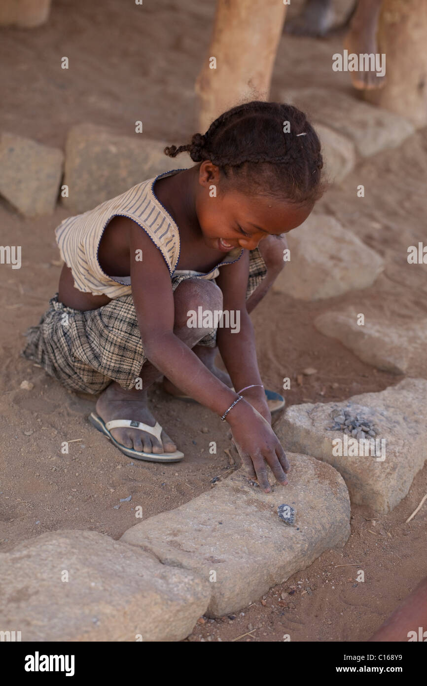 Petite fille casser ou knapping et à l'écaillement des pierres. Mimmicking profession des parents pour la réparation des routes et de la construction. La province de Fianarantsoa. Madagascar. Banque D'Images