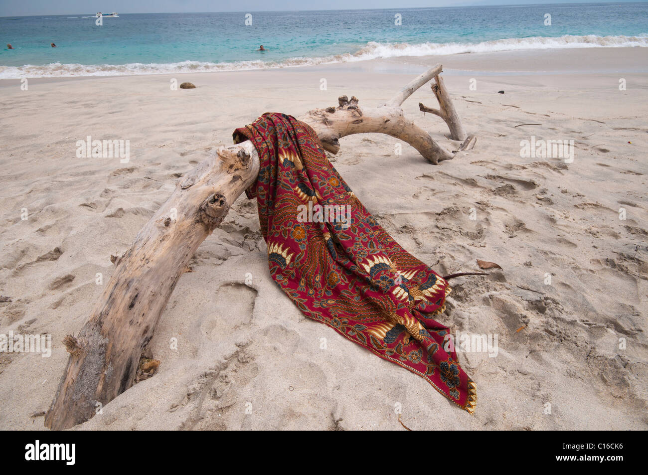 Un sarong batik drapé sur Journal de bois flotté sur la plage de partialité Tegal à Padang Bai Bali Indonésie Banque D'Images