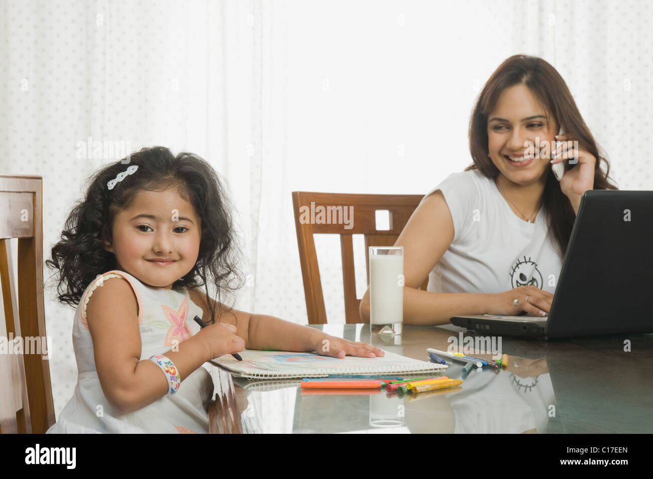 Fille d'une photo et sa mère à l'aide d'un ordinateur portable à côté d'elle à la table à manger Banque D'Images