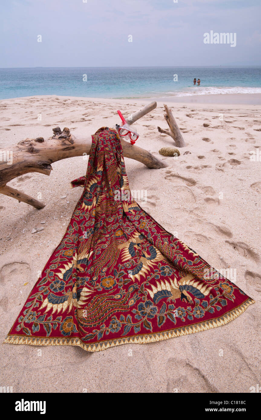 Un sarong batik drapé sur un journal de bois flotté sur la plage de sable blanc de biais Tegal à Padang Bai, à Bali Banque D'Images