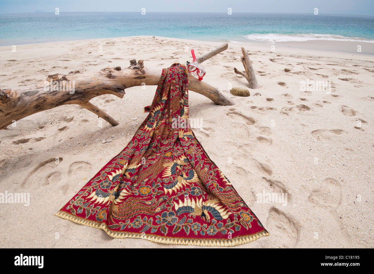 Un sarong batik drapé sur un journal de bois flotté sur la plage de sable blanc de biais Tegal à Padang Bai, à Bali Banque D'Images