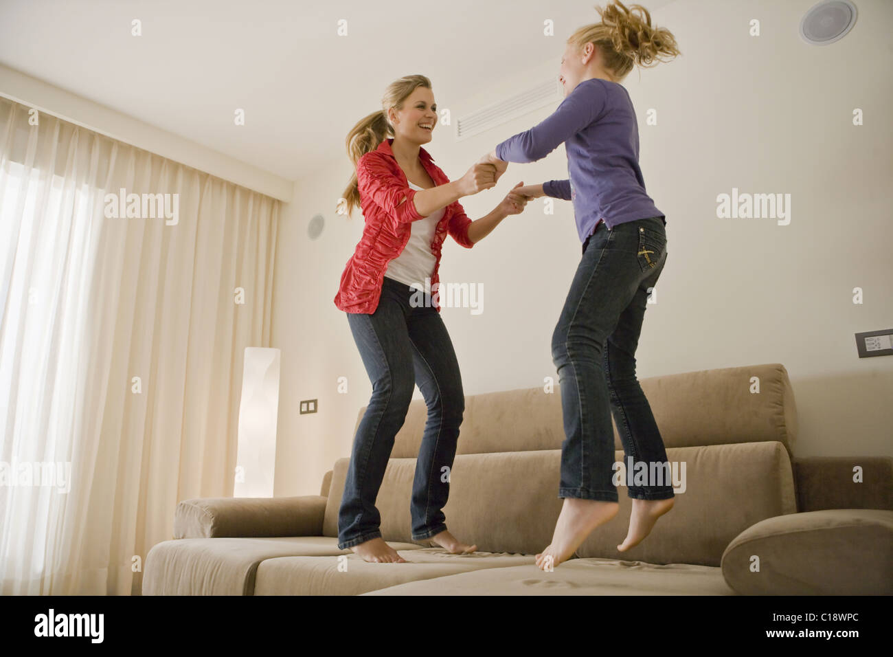 Jeune femme et jeune fille sautant sur canapé Banque D'Images