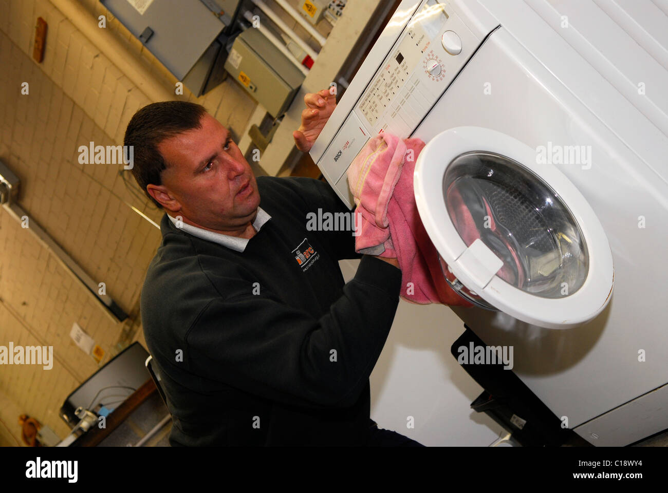 L'homme en bas de nettoyage lave-linge recyclées pour la revente, Clacton, Essex, Royaume-Uni. Banque D'Images