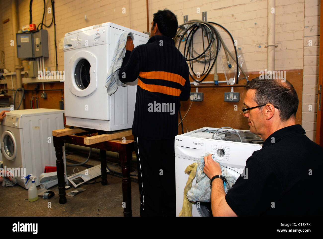 Les hommes en bas de nettoyage des machines à laver recyclé pour la revente, Clacton, Essex, Royaume-Uni. Banque D'Images