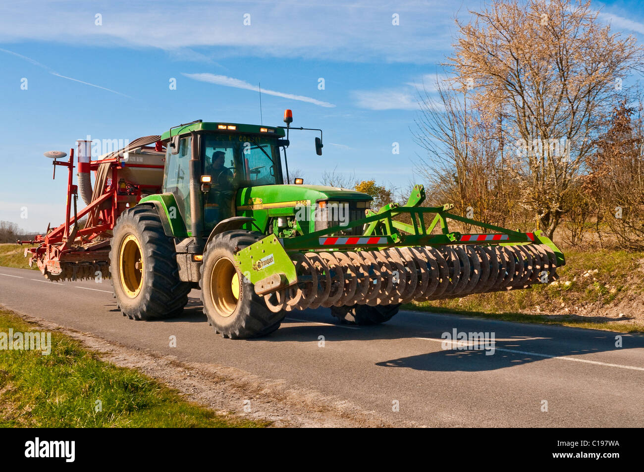 John Deere 8300 tracteur et herses à disques sur voie publique étroite - France. Banque D'Images
