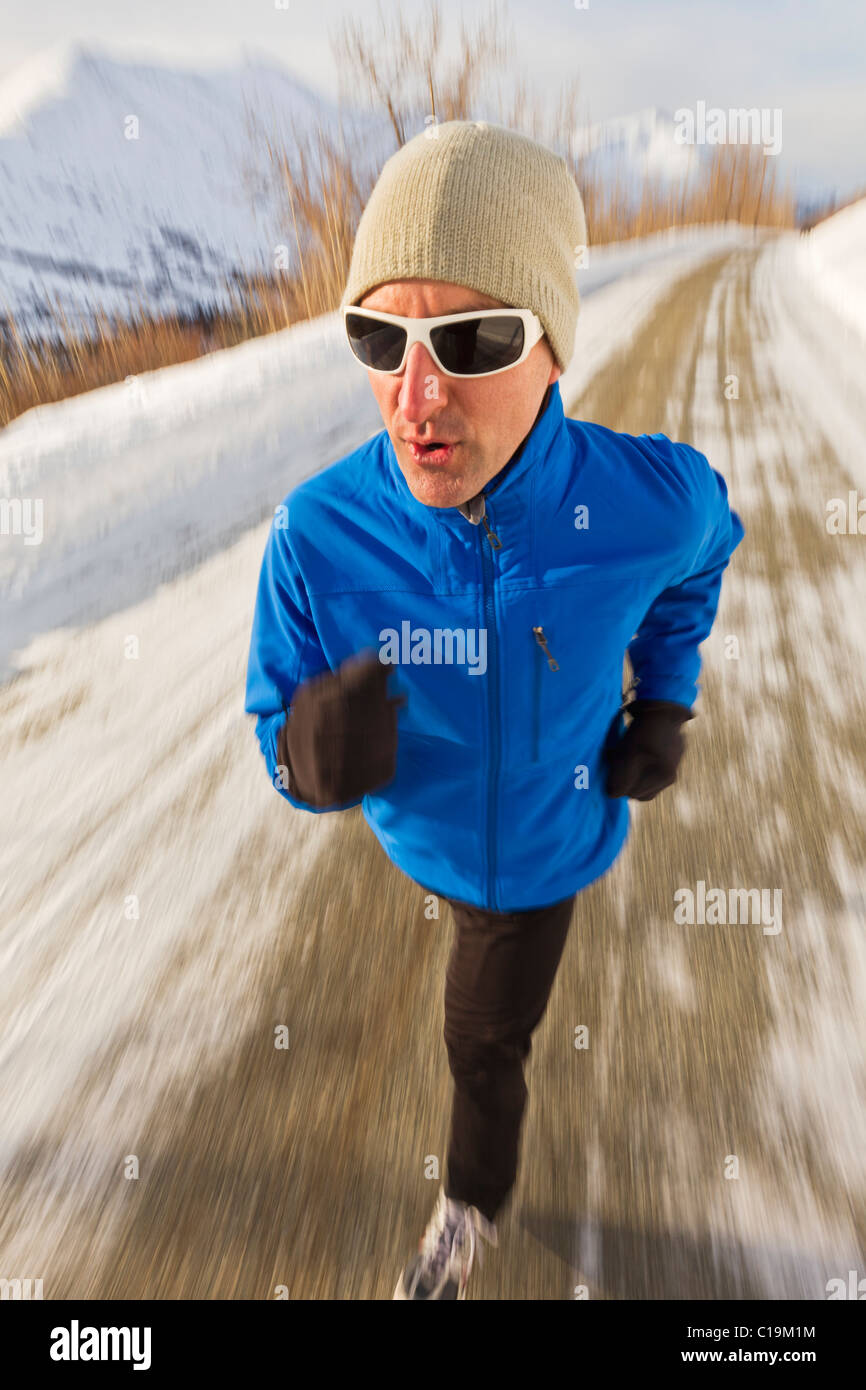 Un homme jogger le jogging le long de la route en hiver en Alaska avec des montagnes en arrière-plan. Banque D'Images