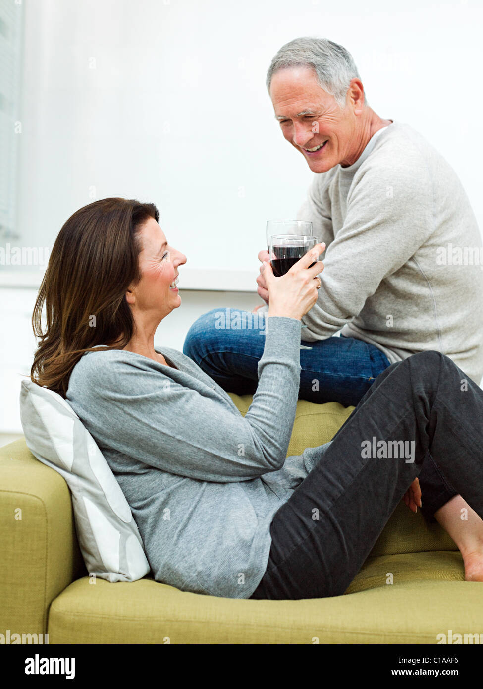 Mature couple sitting on sofa with wine Banque D'Images