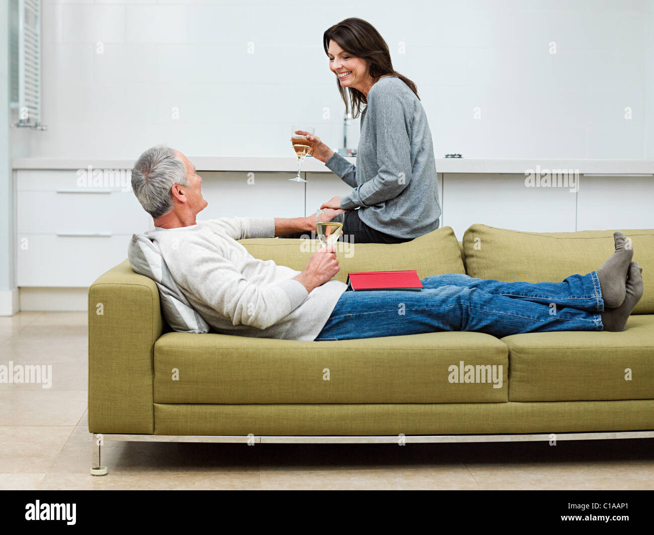 Mature couple sitting on sofa with wine Banque D'Images