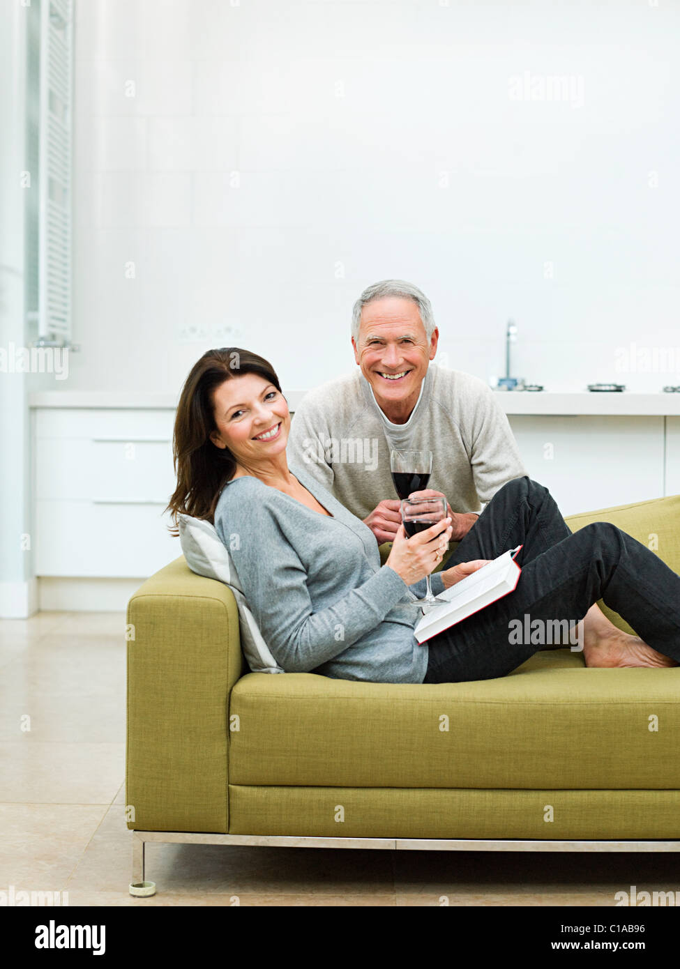 Mature couple sitting on sofa with wine Banque D'Images