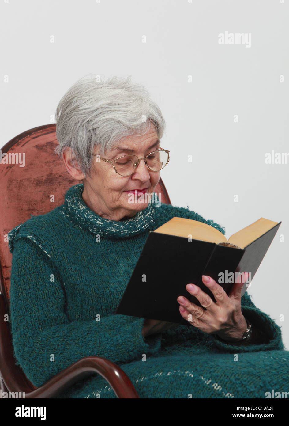 Portrait d'une vieille femme à la lecture d'un livre noir sur fond gris. Banque D'Images
