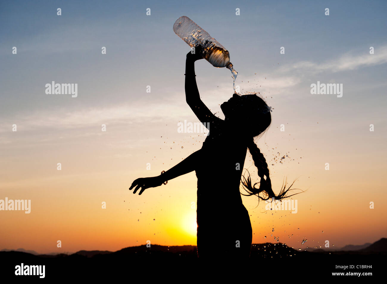 Indian girl se rafraîchir avec de l'eau embouteillée au coucher du soleil. L'Inde. Silhouette Banque D'Images