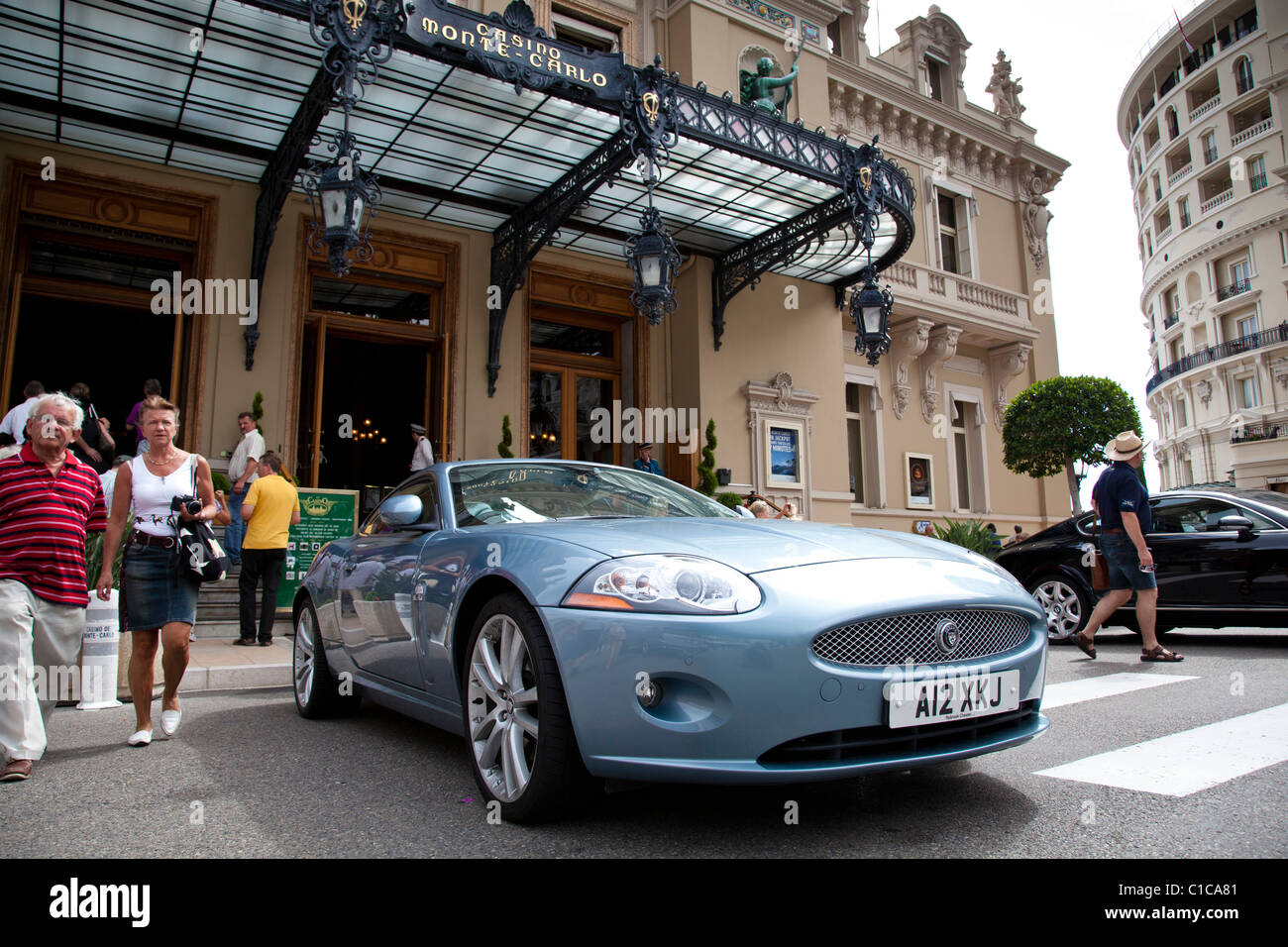 Les touristes viennent et passer par l'entrée au Casino de Monte-Carlo, le remplir avec un coûteux Jaguar garée à l'extérieur. Banque D'Images