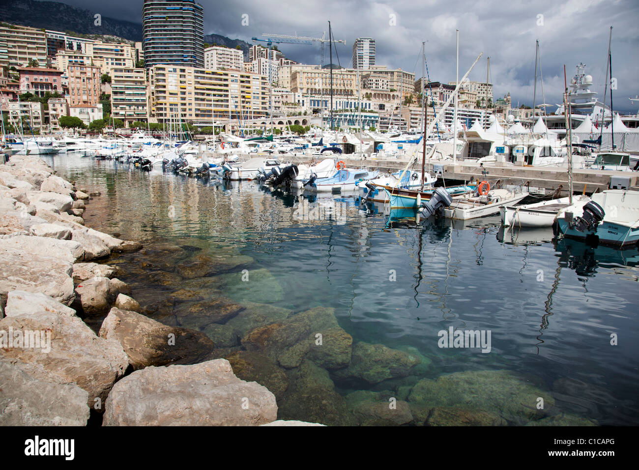 Le port de Port Hercule à Monaco avec les roches et l'eau claire en avant-plan. Banque D'Images