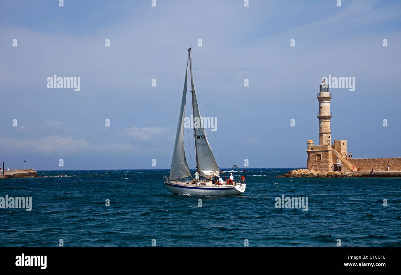 Yacht à quitter le port de Chania le phare de l'Europe avec en arrière-plan Banque D'Images