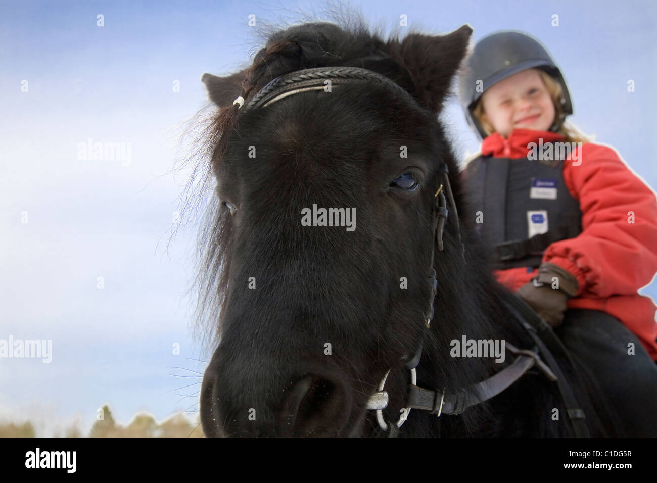 Jeune fille heureuse sur un poney noir. Banque D'Images