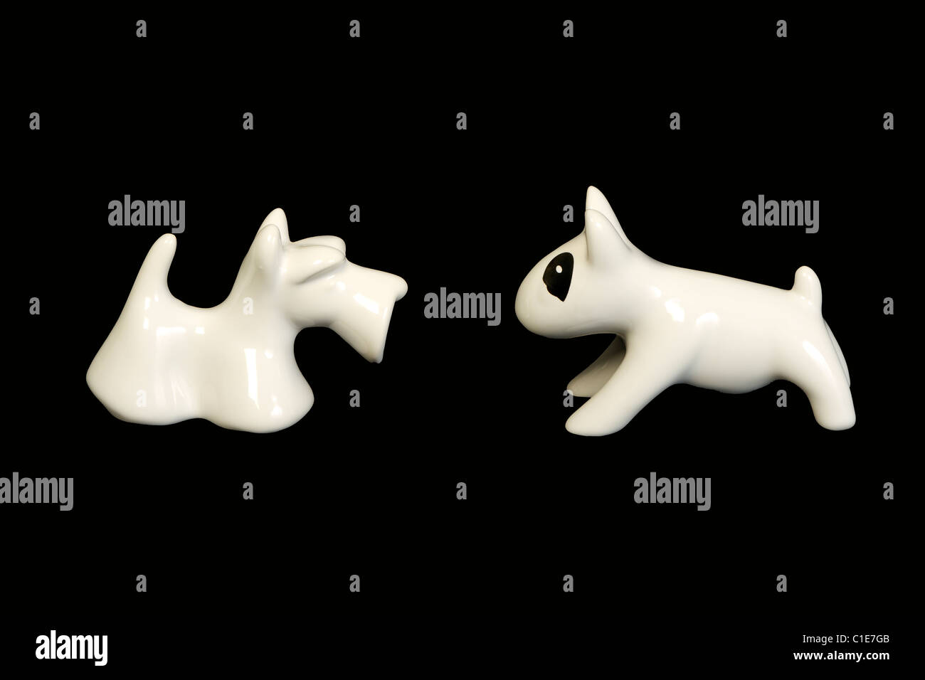 Deux chiens, céramique blanc bull terrier avec tache blanche et scottish terrier confrontés et isolé sur fond noir Banque D'Images