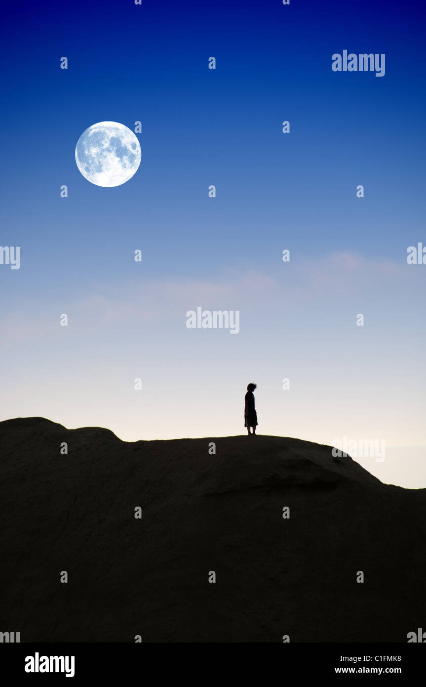Silhouette de garçon sur la colline parlementaire à la tombée de la nuit avec lune derrière lui. Banque D'Images