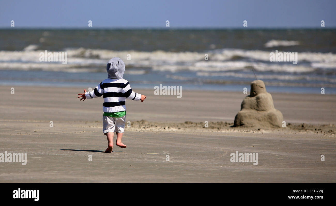 Un petit garçon s'exécute à un château de sable sur la plage à Kiawah Island, SC. Banque D'Images