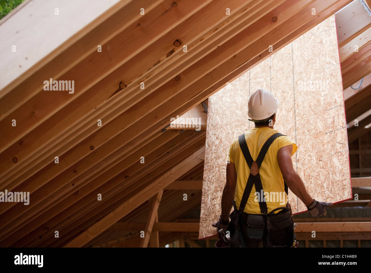 Hispanic carpenter poussant jusqu'à revêtement de toit à une maison en construction Banque D'Images