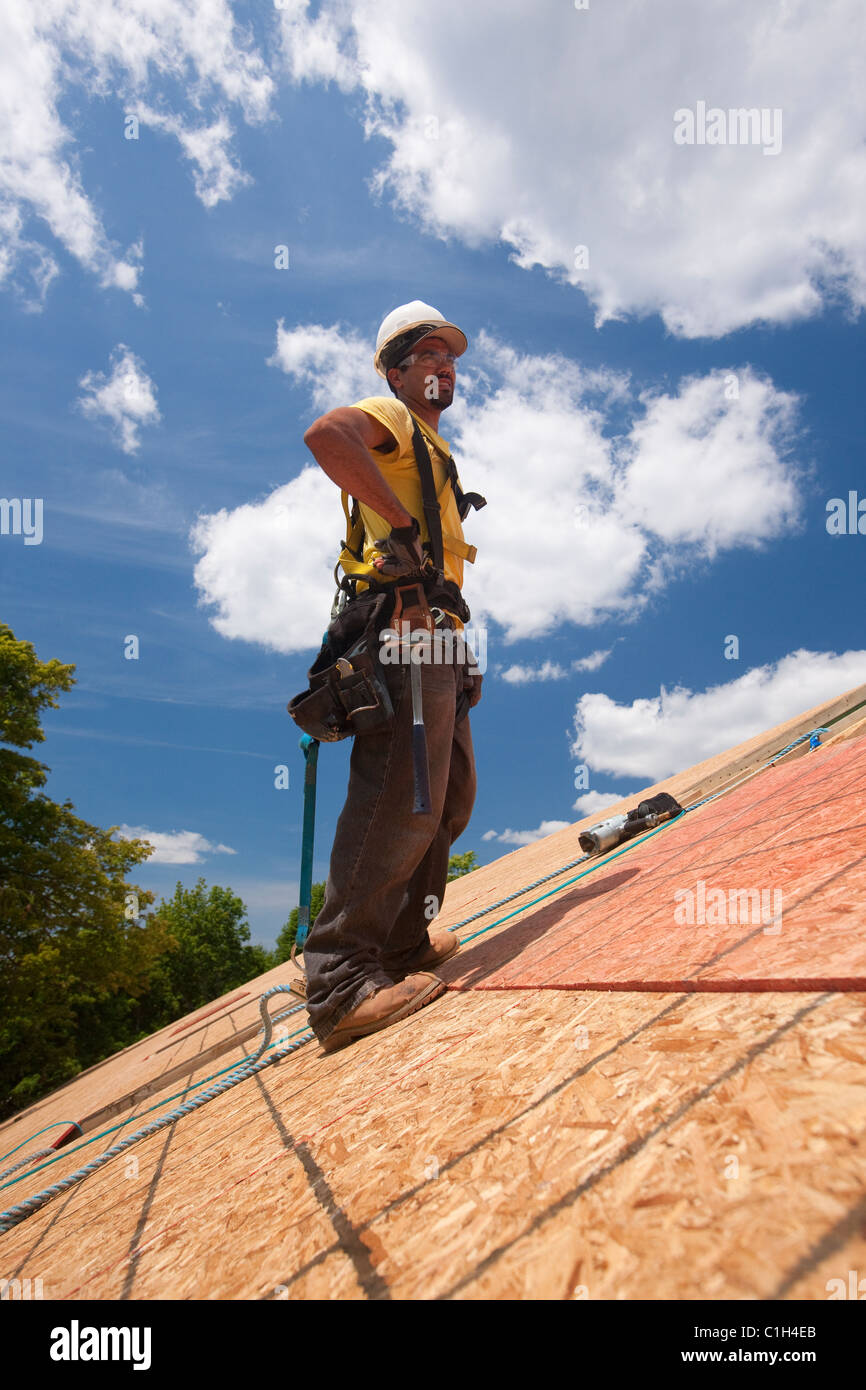 Hispanic carpenter debout sur le toit d'une maison en construction Banque D'Images