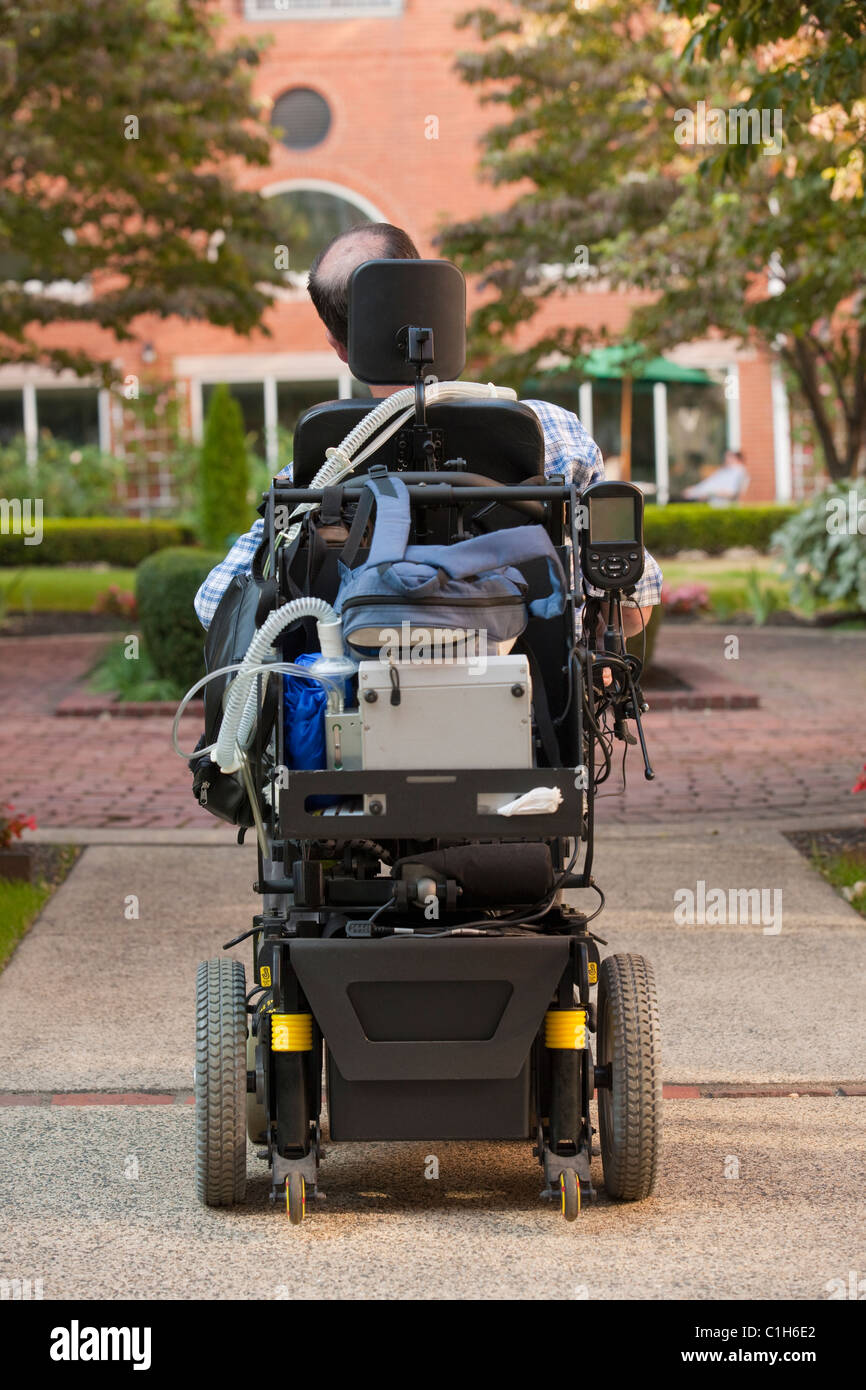 Vue arrière d'un homme ayant la dystrophie musculaire de Duchenne dans un fauteuil roulant motorisé sur la rue Banque D'Images