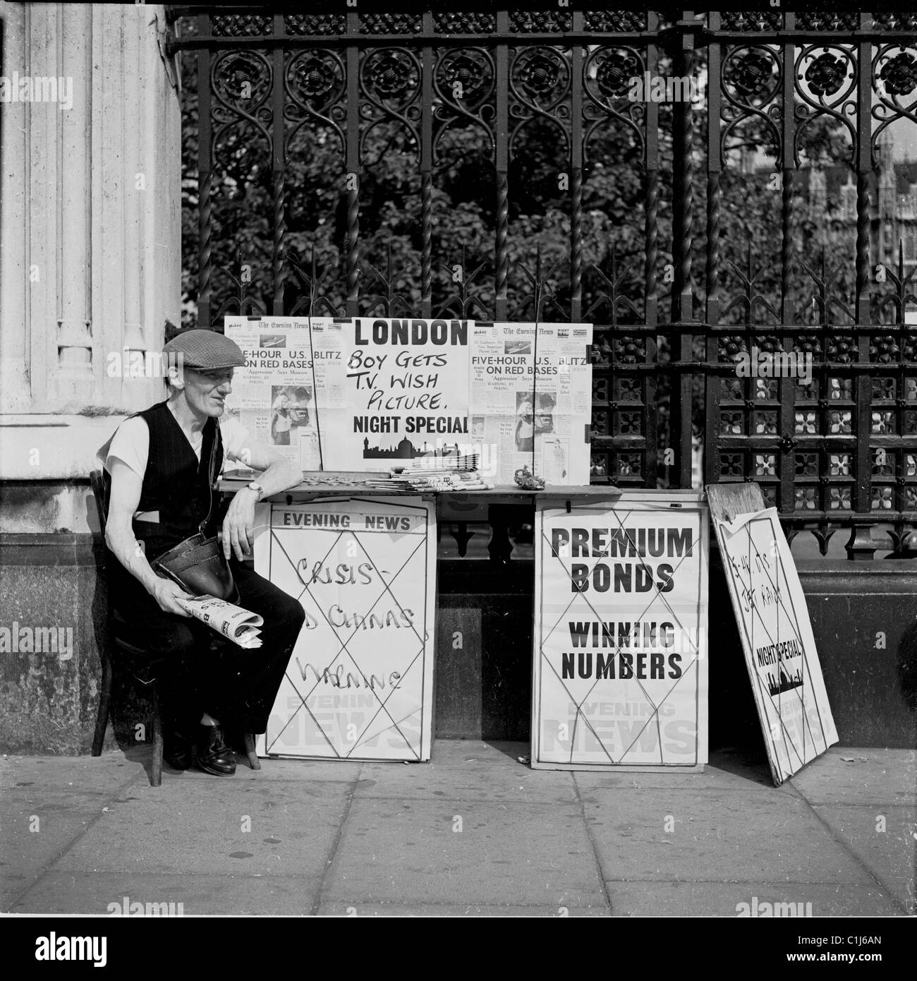 1950s, un vendeur à casquette plate, tenant un journal, assis sur une petite chaise sur le trottoir, vendant le journal du soir de Londres, The Evening News Banque D'Images
