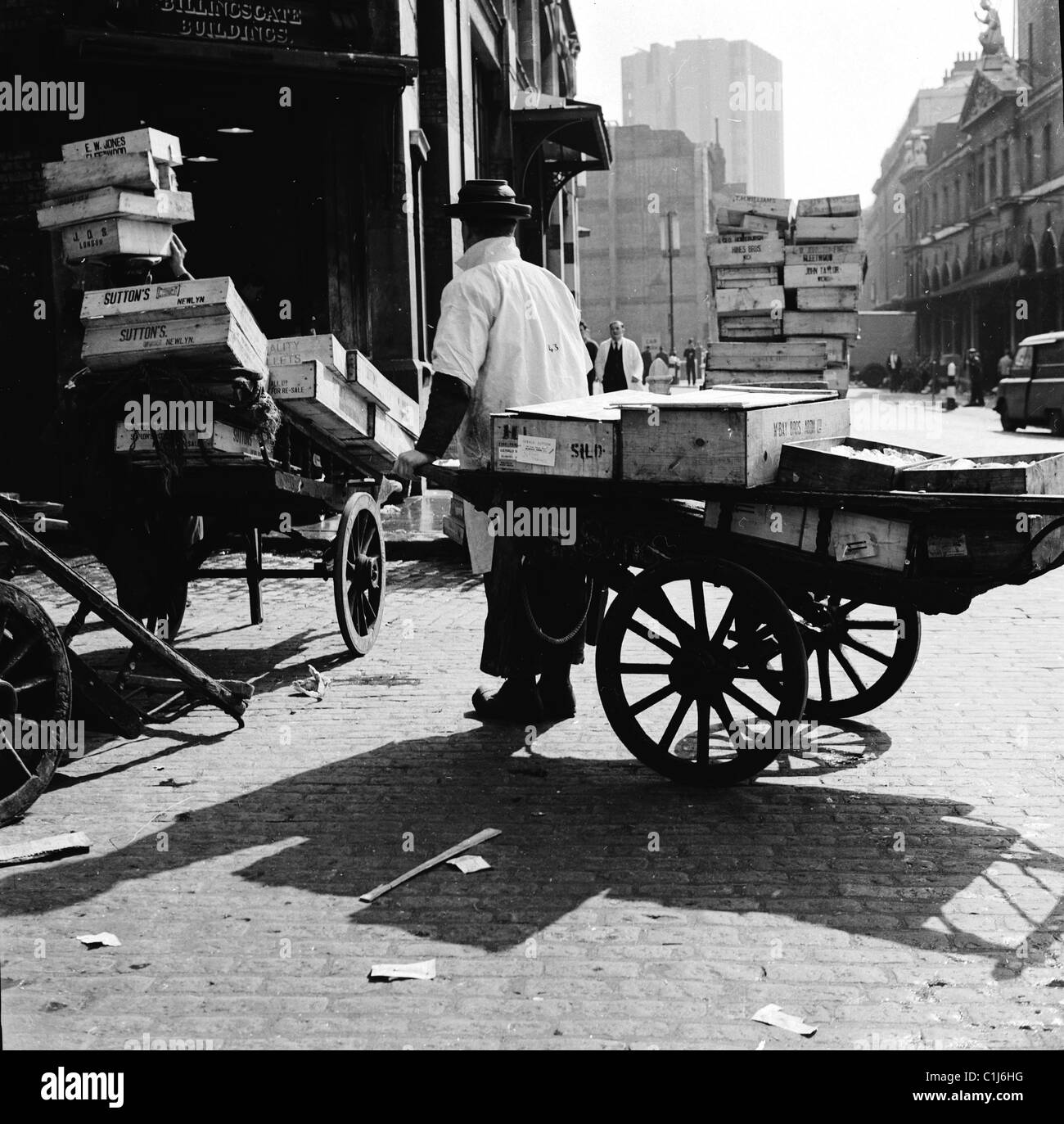 1950s, un portier au célèbre marché aux poissons de Billingsgate tirant un chariot en bois chargé de caisses de poisson congelé à Lower Thames St, Londres, Angleterre. Banque D'Images