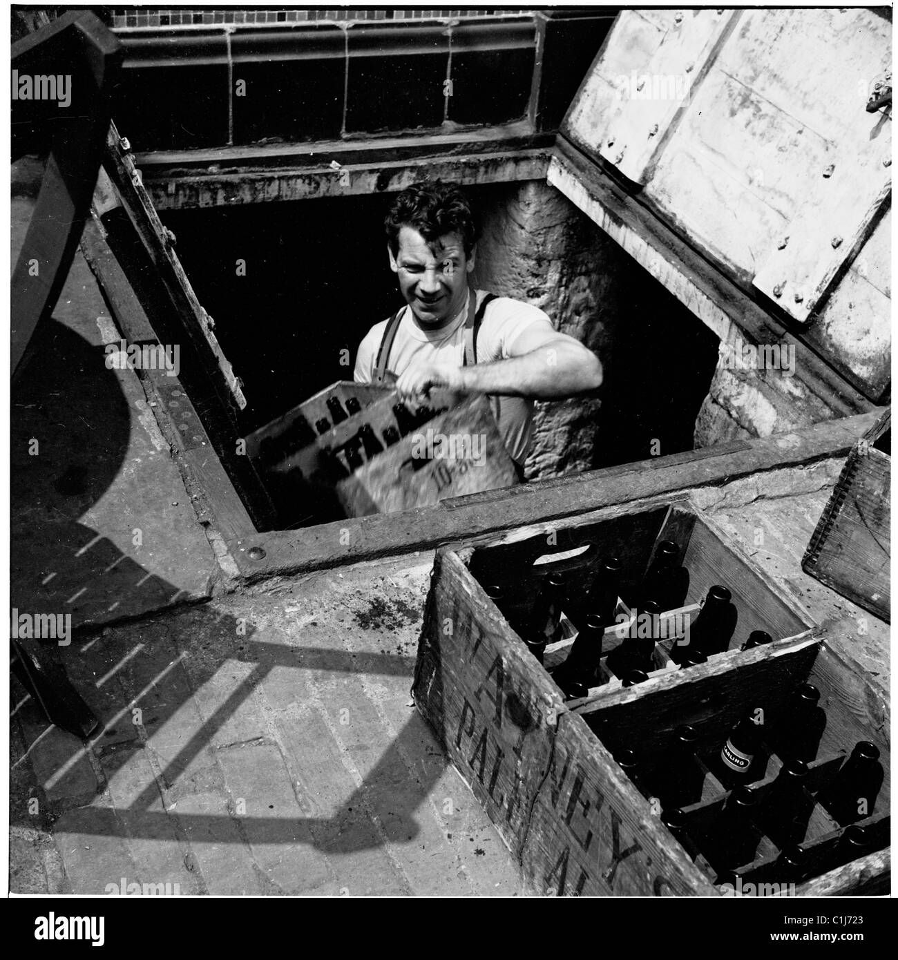 Dans les années 1950, un ouvrier de brasserie apporte des caisses de bouteilles vides d'une cave située sous la rue, à Londres, en Angleterre, au royaume-uni. Banque D'Images