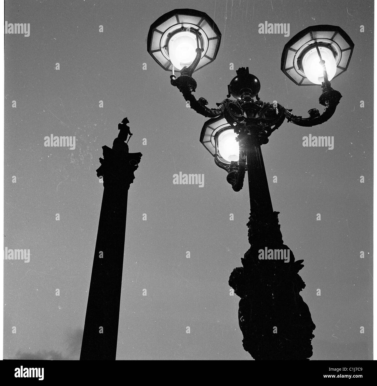 Années 1950, la nuit et les lampadaires décoratifs en fer éclairent la statue emblématique de la colonne de Nelson à Traflagar Square, Westminster, Londres, Angleterre. Banque D'Images