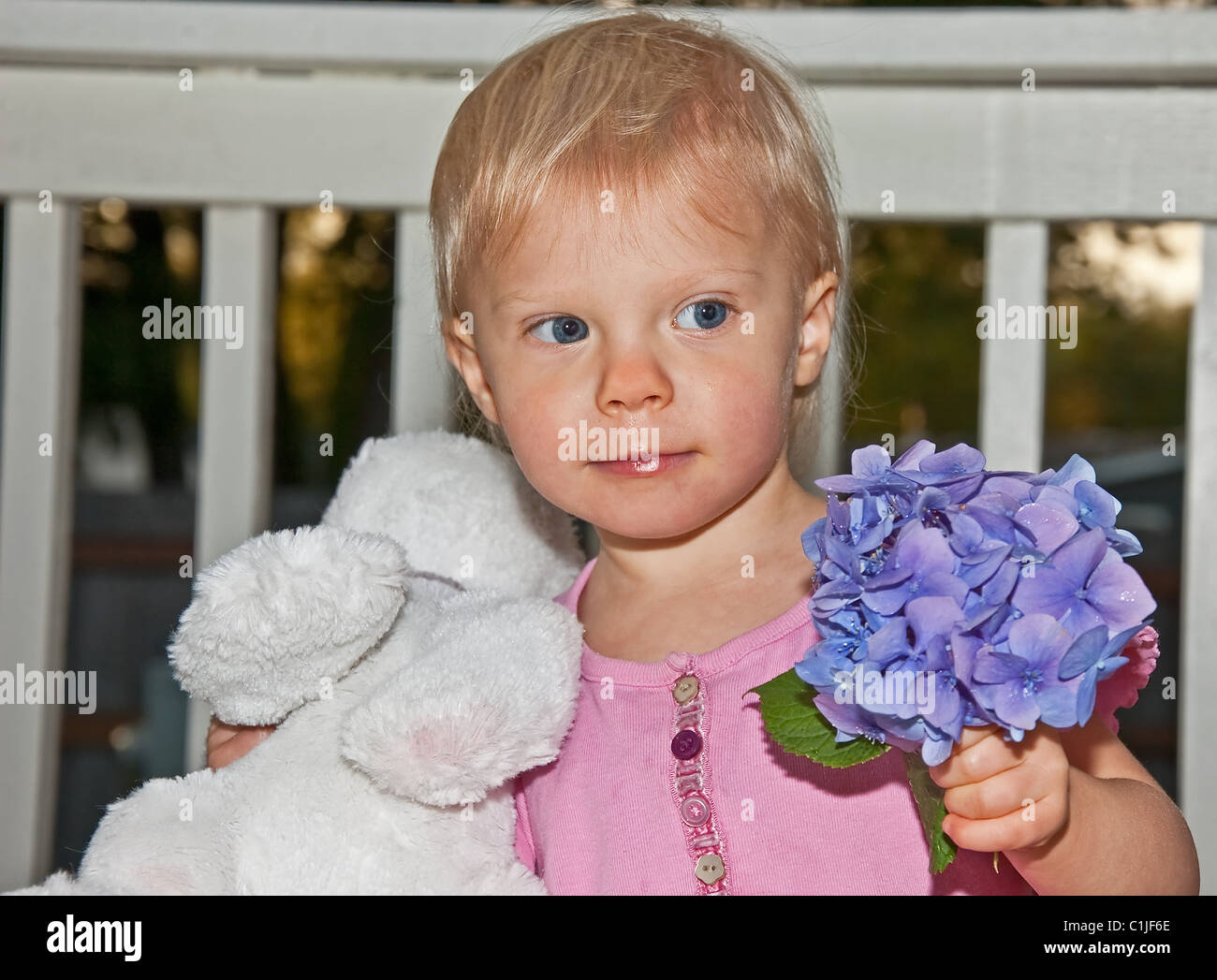 Ce mignon, Caucasian girl holding est un animal en peluche et un hortensia fleur tandis qu'à l'extérieur au crépuscule. Banque D'Images