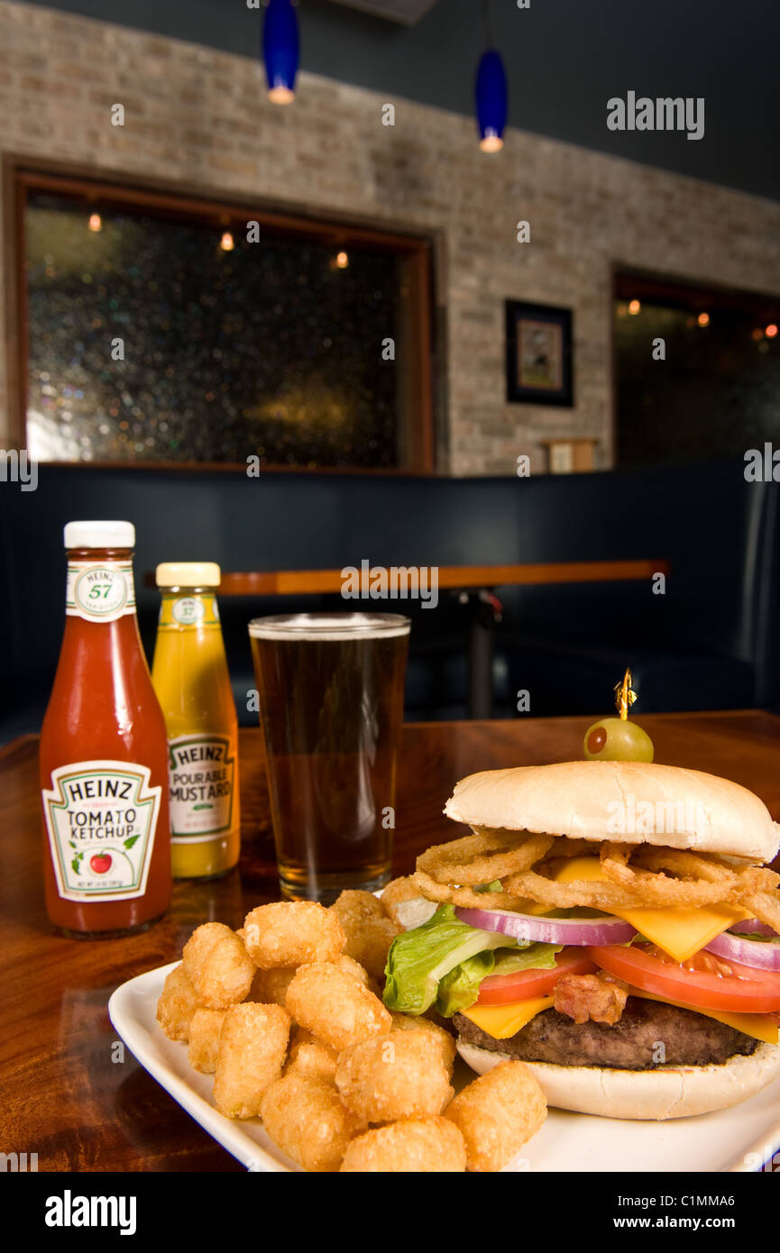 Hamburger de luxe, tater tots, et bière servi dans un restaurant. Banque D'Images