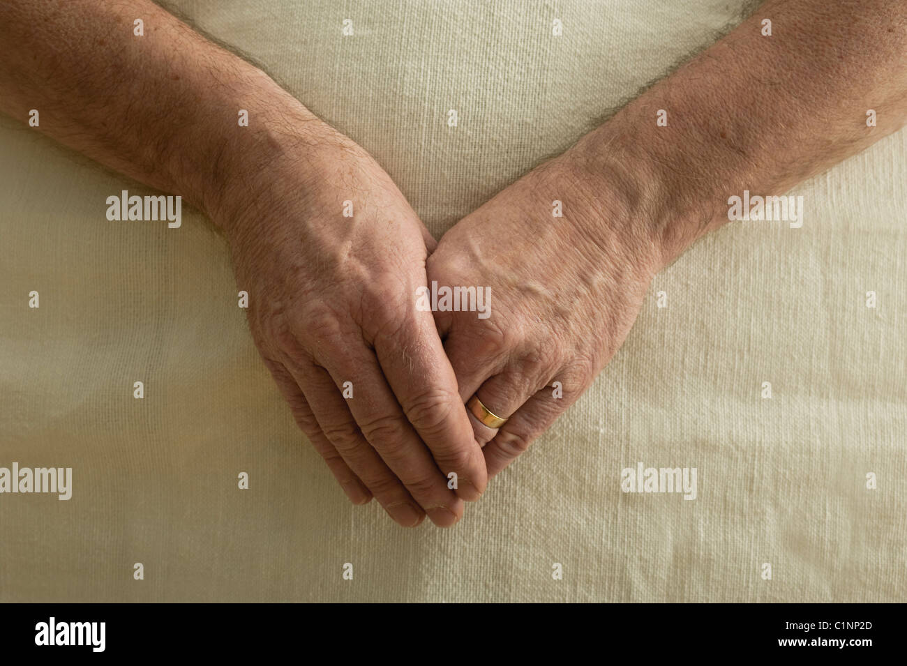 Un homme légèrement les mains jointes devant lui, sur un couvre-lit Banque D'Images
