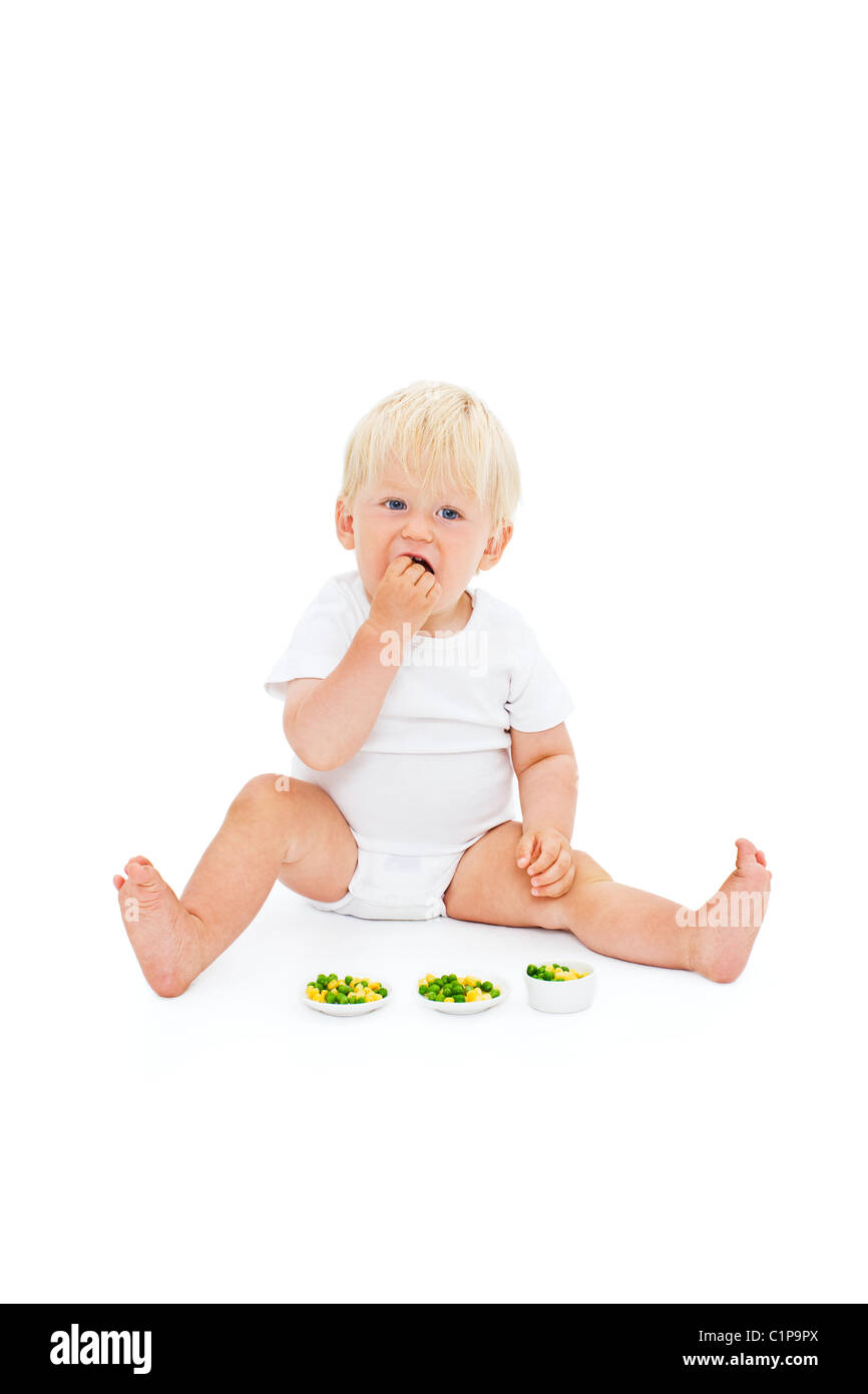 Studio shot of baby boy eating peas Banque D'Images