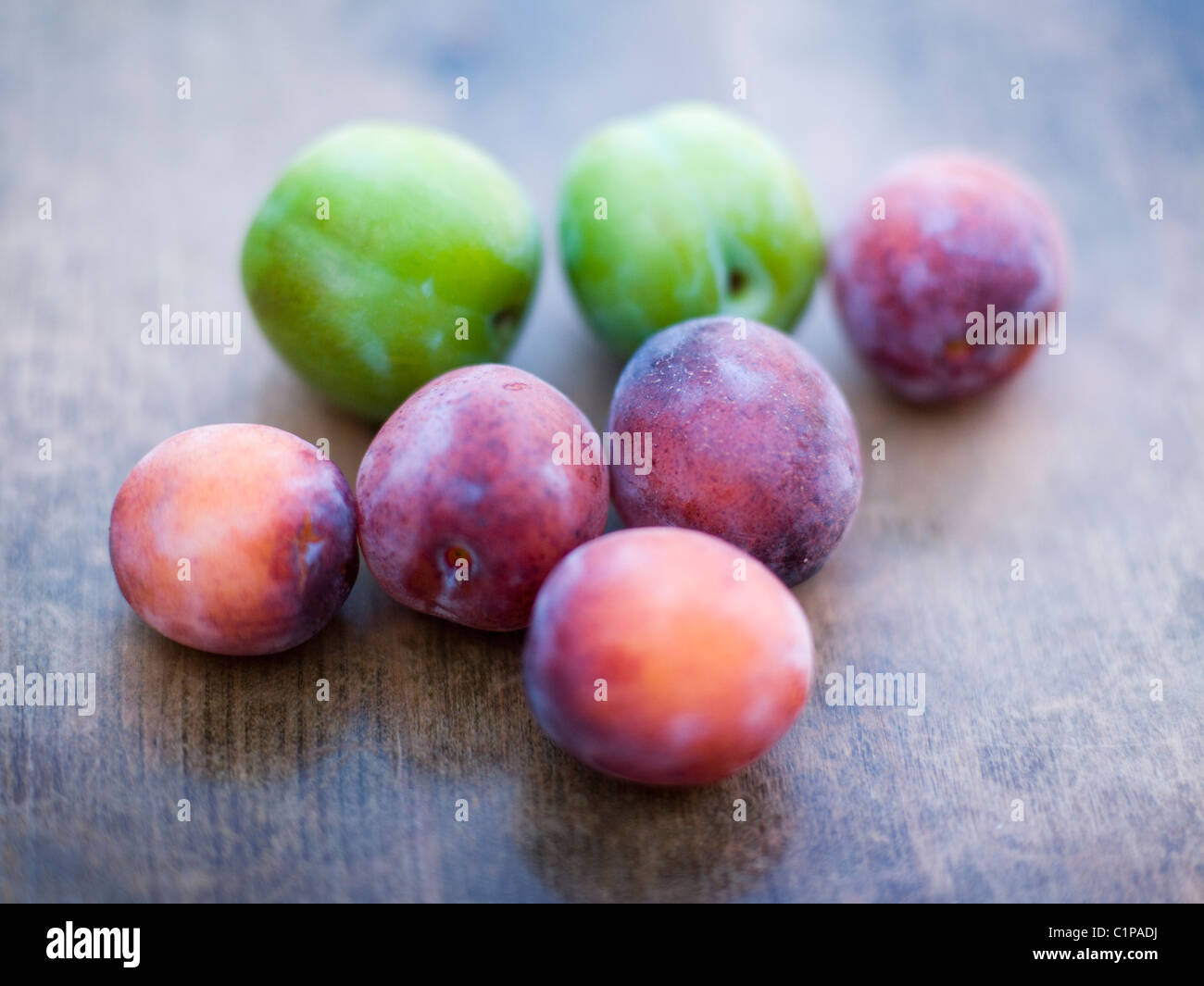 Les prunes vertes et violettes sur table en bois Banque D'Images
