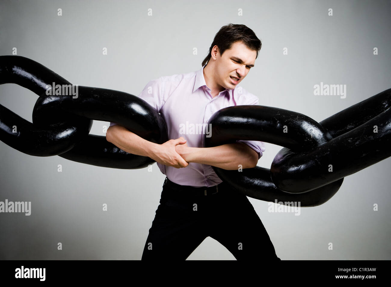 Portrait of businessman tendue avec deux sections d'énorme chaîne sur fond gris Banque D'Images