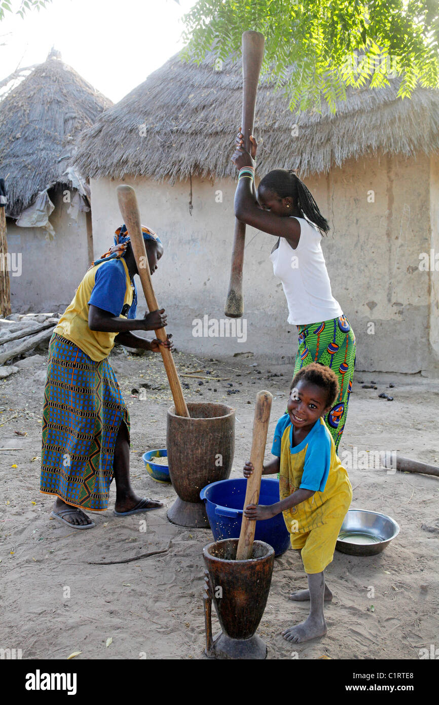 Femme et enfant battre le mil, maïs, sorgoum à l'aide de mortier et pestel. Sénégal Banque D'Images