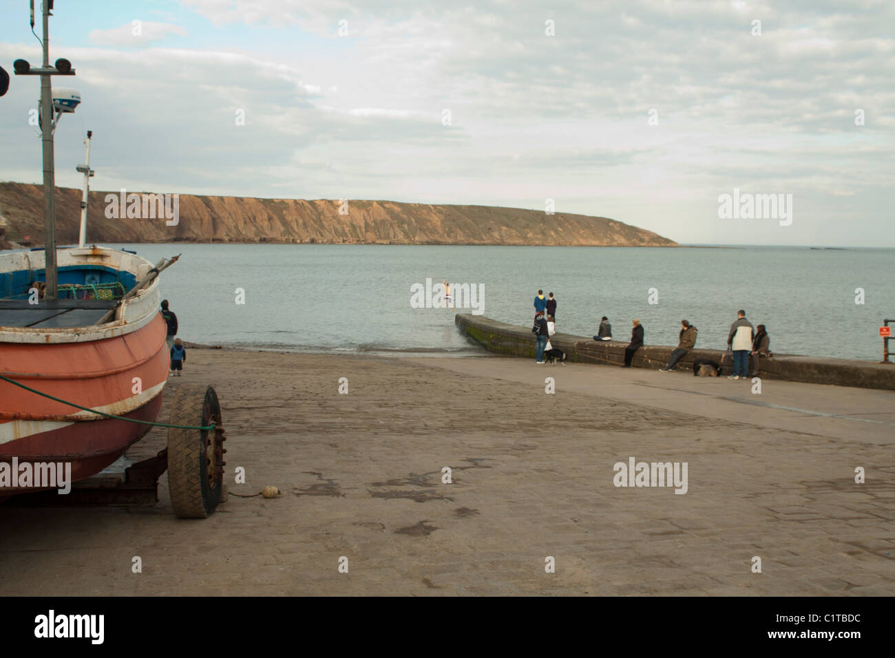 Jeune garçon plongeant dans la mer à l'atterrissage avec le Coble Filey Country Park Cliffs et le Brick à l'arrière-plan Banque D'Images