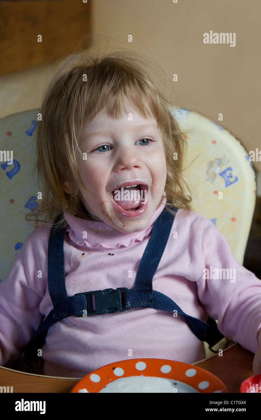 Sale heureux deux ans caucasien enfant fille assise et crier d'une chaise haute Banque D'Images