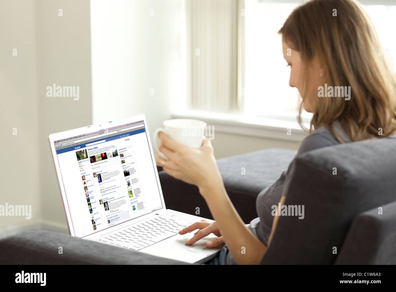 Femme se prélasser dans le salon lors de la vérification de son compte Facebook sur un ordinateur portable Banque D'Images