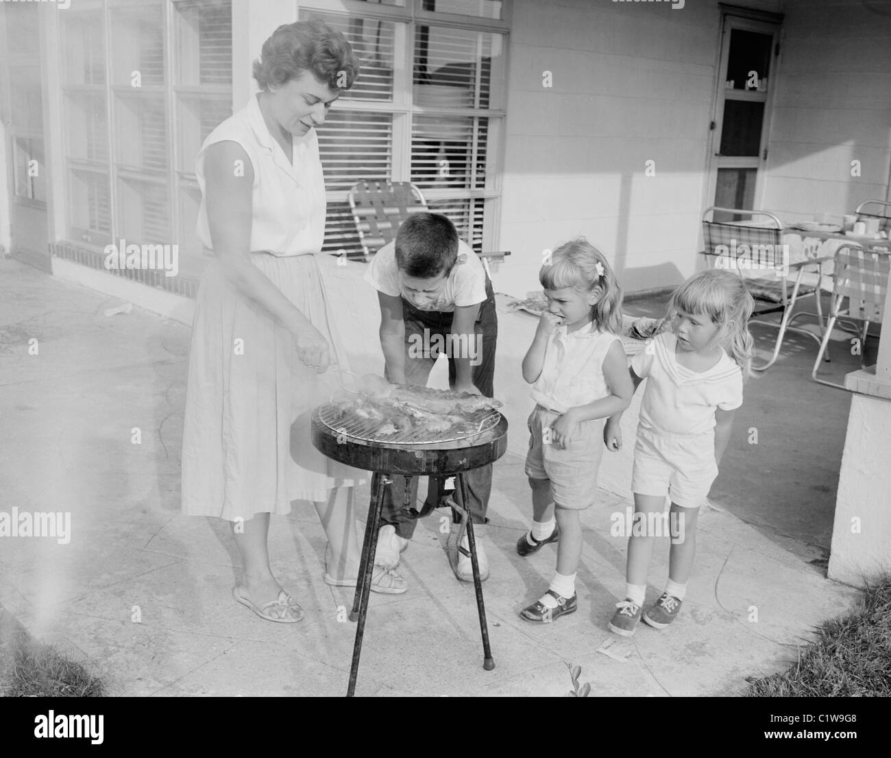 Mère de faire un barbecue et les enfants la regarder Banque D'Images