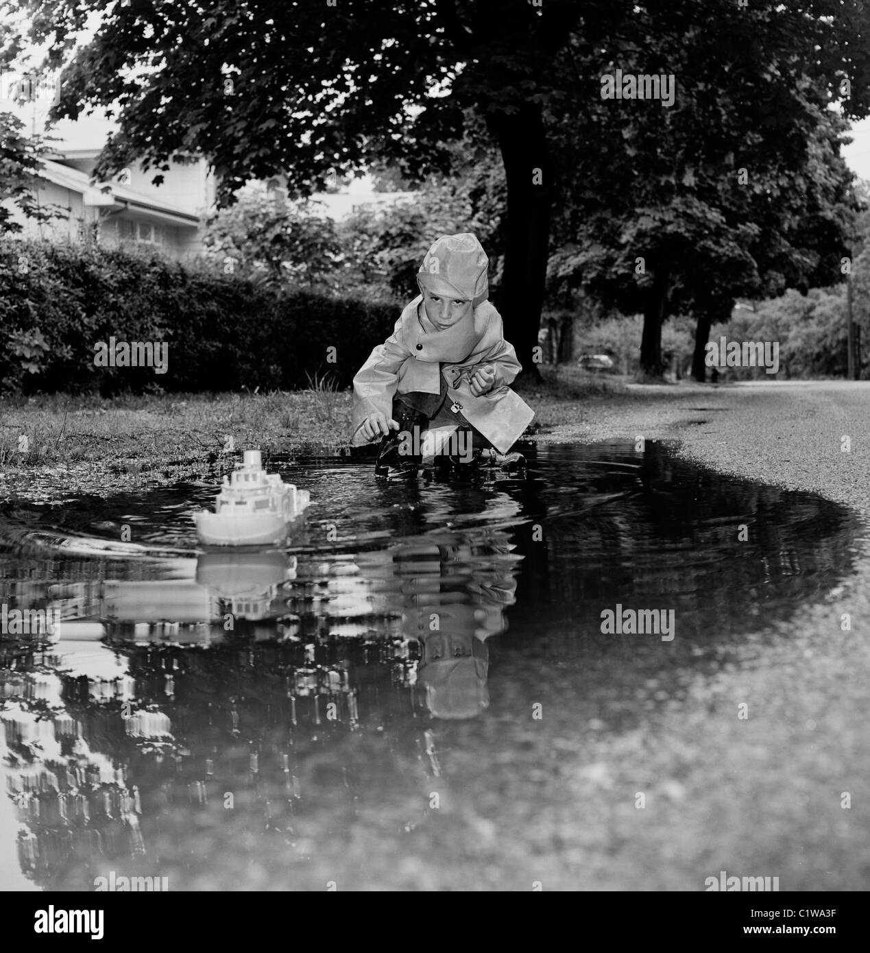 Boy Playing with toy boat in puddle Banque D'Images