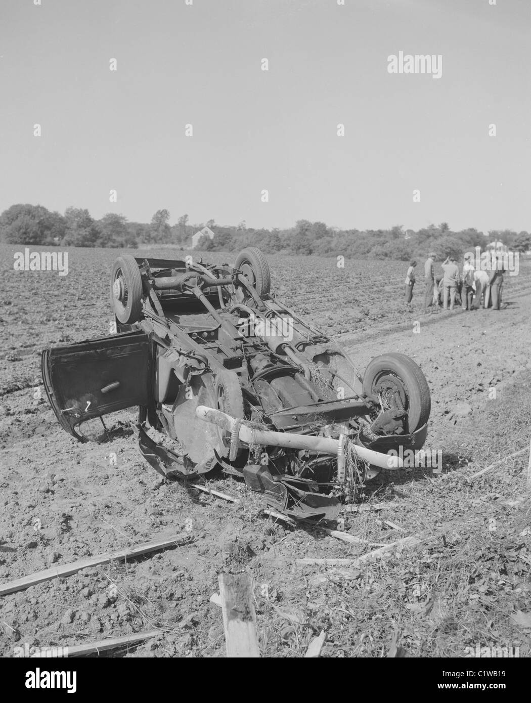 Voiture renversée dans un champ, la foule rassemblée près de blessés. Banque D'Images