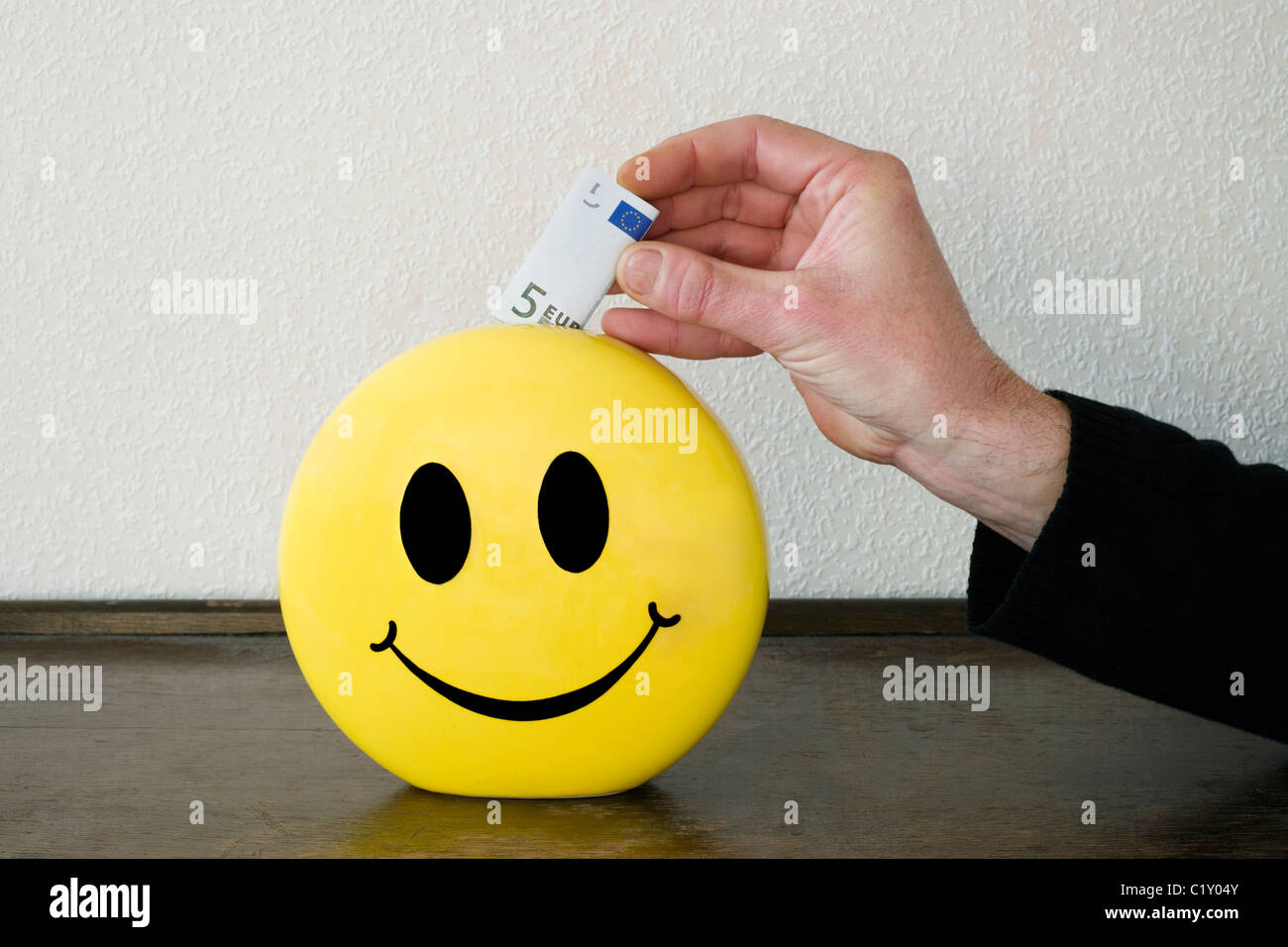L'homme mettant l'argent dans une boîte d'épargne smiley Banque D'Images