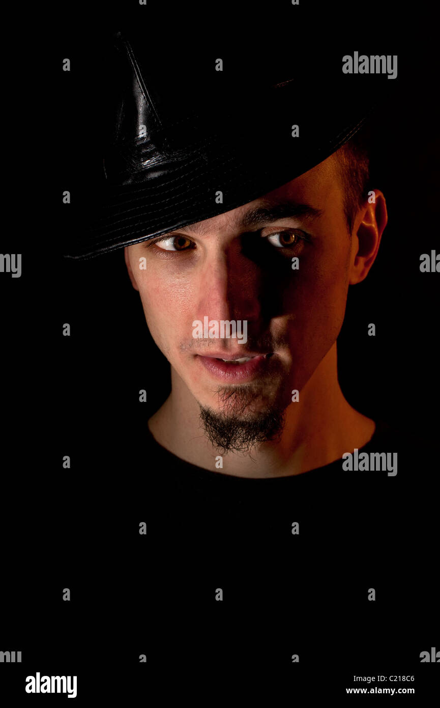 Portrait de studio de surpris bel homme en chapeau sur fond noir. Image clé faible éclairage rouge utilisé Banque D'Images