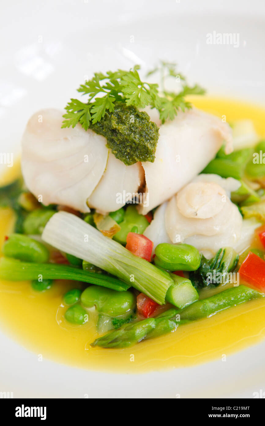 Lotte à la vapeur sur un lit de légumes verts avec une sauce beurre blanc. Banque D'Images