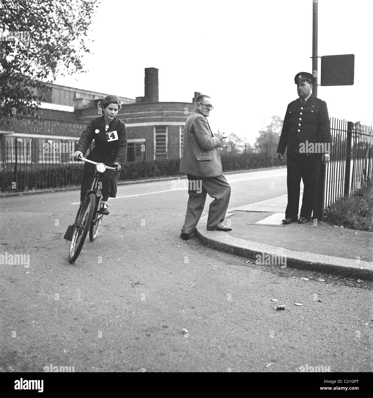 1950s, historique, debout sur un trottoir au coin d'une route, un policier regarde une écolière faire son test de maîtrise du cyclisme, Angleterre, Royaume-Uni. Banque D'Images