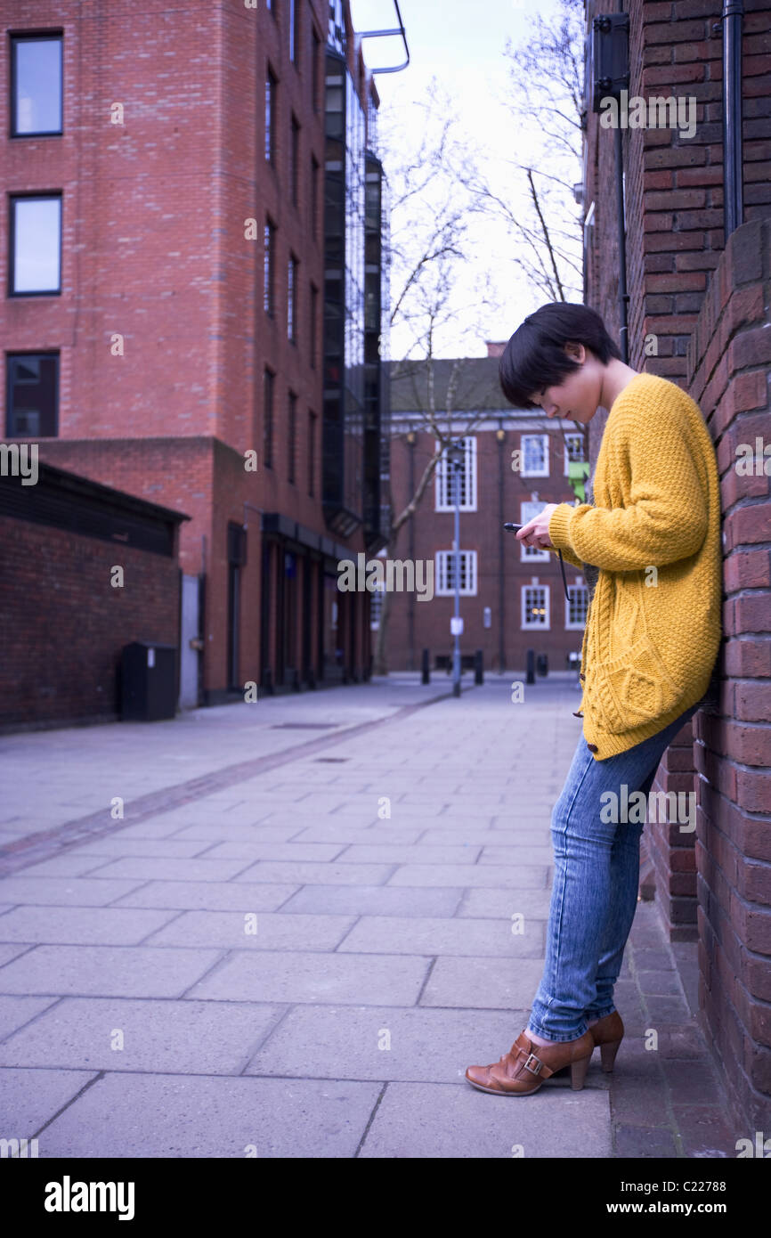 Une jeune femelle adulte en utilisant son téléphone tout en s'appuyant sur le mur Banque D'Images