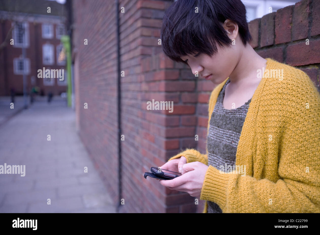 Une jeune femelle adulte en utilisant son téléphone tout en s'appuyant sur le mur Banque D'Images