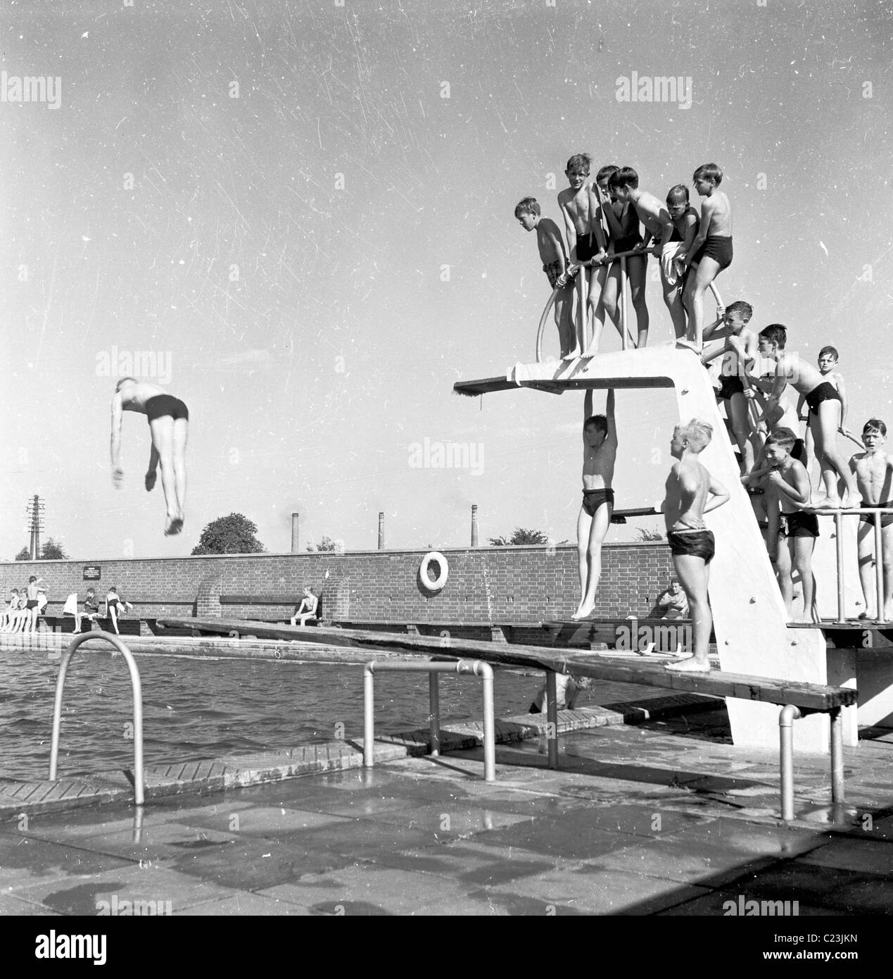 Angleterre, années 1950. Photographie par J Allan Paiement d'un groupe de garçons sur la plate-forme à une piscine extérieure. Banque D'Images